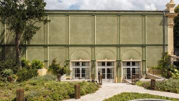 A building with a green lattice facade, large arched windows, and a central entrance with steps.