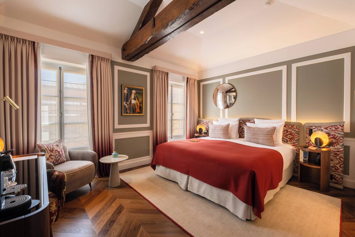 Ruime slaapkamer met een groot bed, een zithoek met een fauteuil, een klein tafeltje en een koffieapparaat.