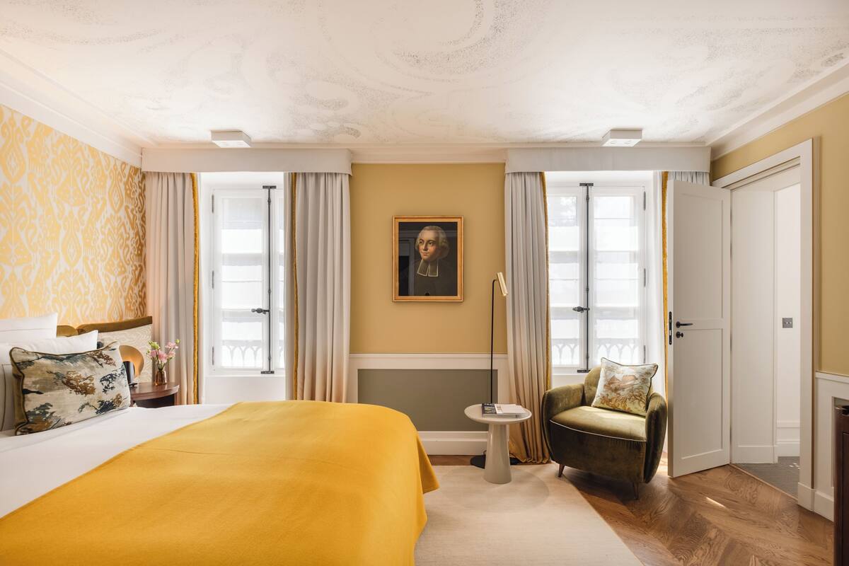 Een hotelkamer met een groot bed, een klein rond tafeltje, een stoel en een schilderij aan de muur.