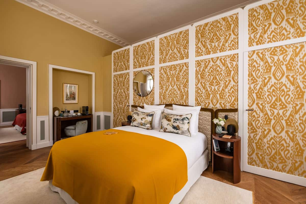 Een slaapkamer met een groot bed, een spiegel erboven en behang met een patroon.