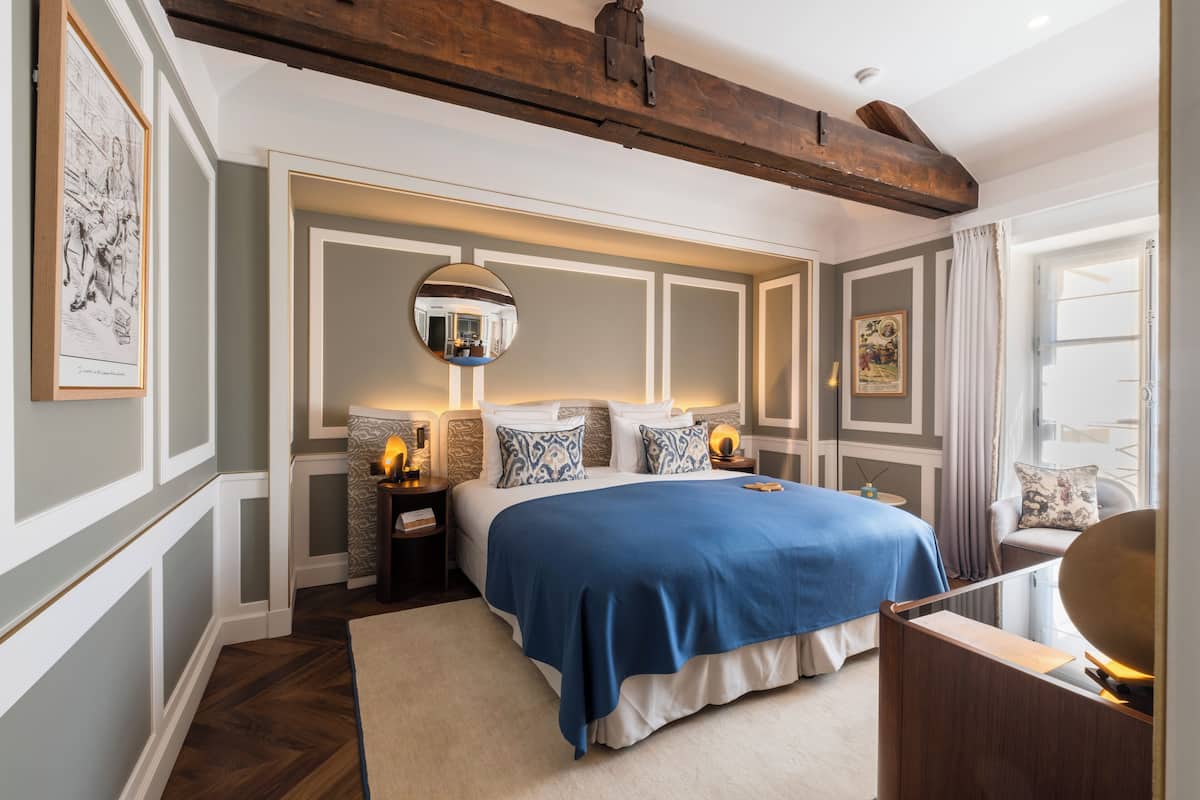 Een slaapkamer met een groot bed, een ronde spiegel, nachtkastjes en een nachtkastje.