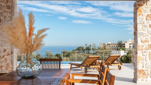 Een terras met een houten tafel, lounge fauteuils en een vaas met pampasgras.