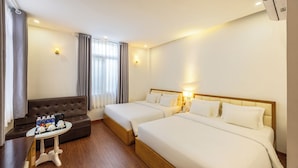 A hotel room with two beds, a sofa, a small table with amenities, and a window with curtains.