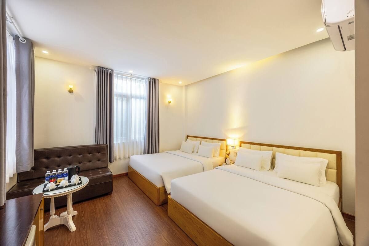 A hotel room with two beds, a sofa, a small table with amenities, and a window with curtains.