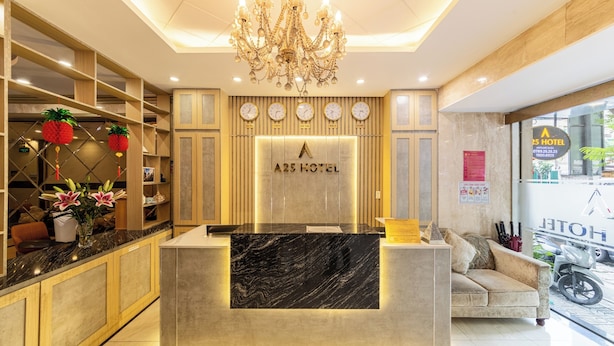 A hotel reception area with a marble counter, a chandelier, clocks, and a sofa.