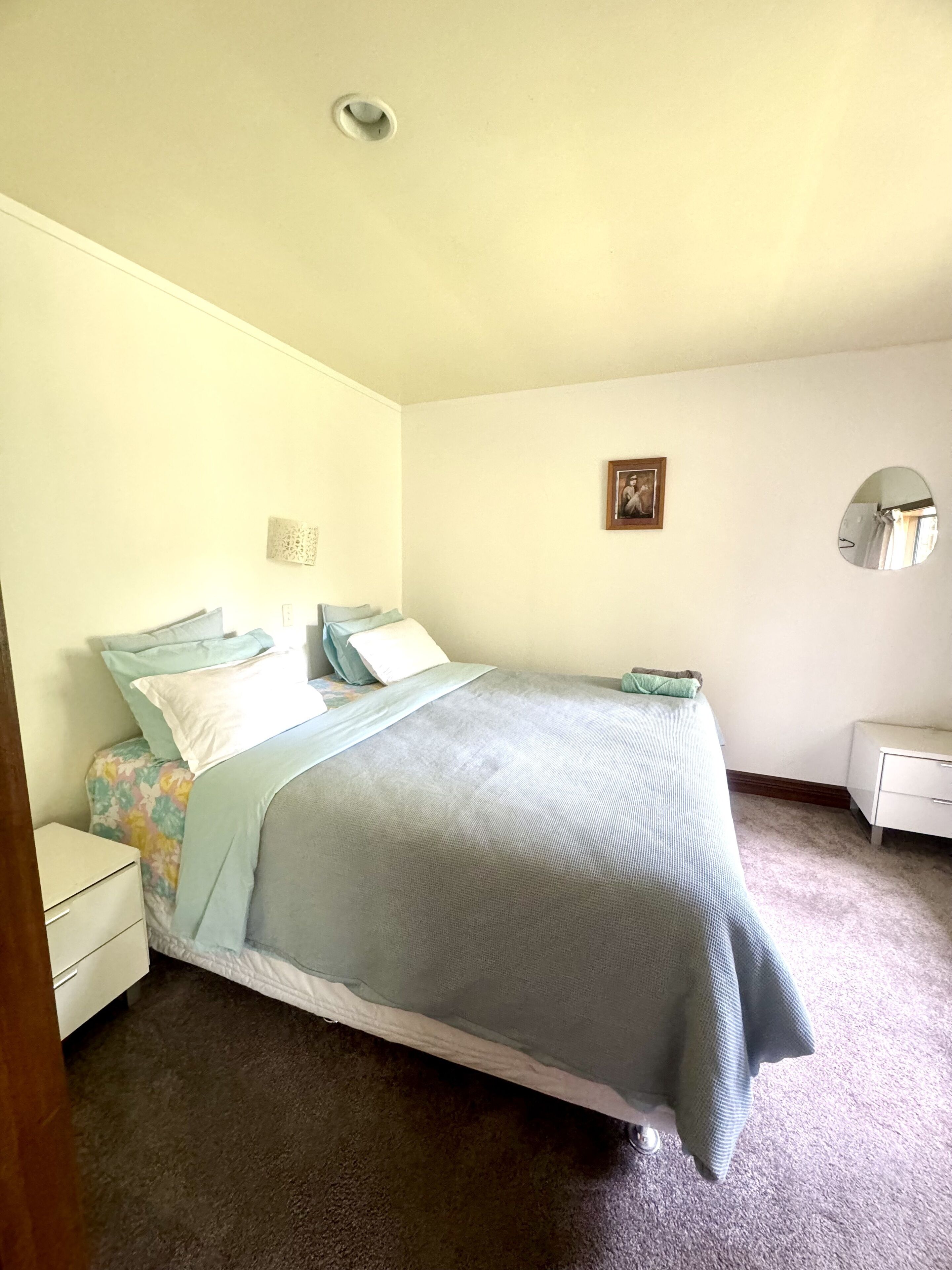 A bedroom with a bed, a nightstand, a dresser, a mirror, and a framed picture on the wall.