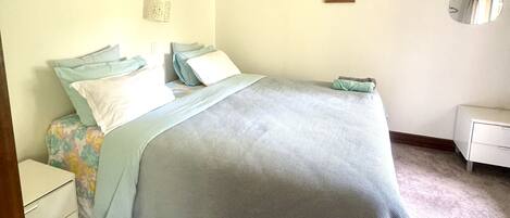 A bedroom with a bed, a nightstand, a dresser, a mirror, and a framed picture on the wall.