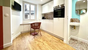 A compact kitchen with a wooden floor, white cabinets, a built-in oven, and a small window.