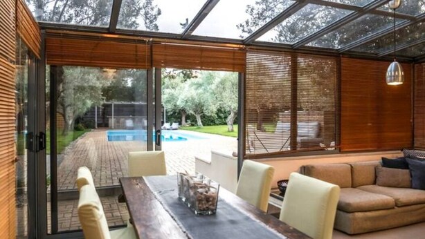 Un interior moderno con una puerta de cristal que da a un espacio exterior, una mesa de comedor de madera y un sofá.