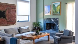 Una sala de estar con sofá, sillones, una mesa de centro, chimenea y dos cuadros en la pared.