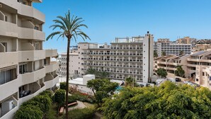 A multi-story residential building with balconies, a palm tree, and surrounding greenery.