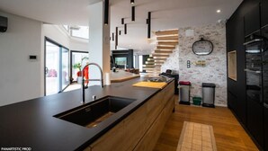 A modern kitchen with a central island, black cabinetry, and a brick accent wall.