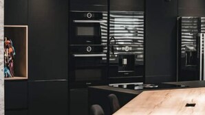 A modern kitchen with black cabinetry, a wooden dining table, and pendant lighting.