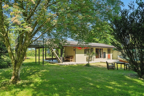 A house with a covered patio, a small deck, and a boat in the background.