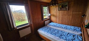 Ein Zimmer in einer Holzhütte mit einem Bett, einem Fenster, einer Heizung und einem Bild an der Wand.