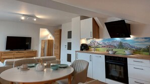 Una cocina moderna con un mural de montañas, un comedor con una mesa redonda y un televisor en la sala.