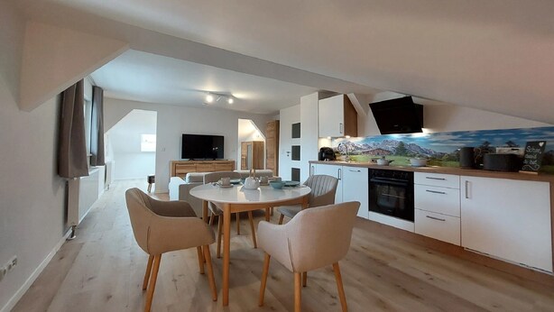 Una cocina moderna con comedor, televisor montado en la pared y un mural decorativo sobre la encimera.