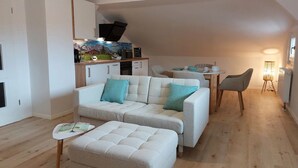 Una sala moderna con sofá, reposapiés y zona de comedor.
