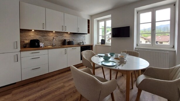 Une cuisine moderne avec des meubles blancs, un pare-feu en pierre et un coin repas comprenant une table ronde et quatre chaises.