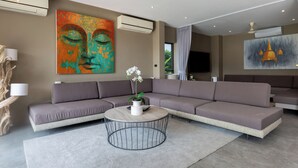 A modern living room with a sectional sofa, a round coffee table with a vase of flowers, and two large abstract paintings on the walls. - Villa Thansamaay by Elite Havens (Koh Samui)