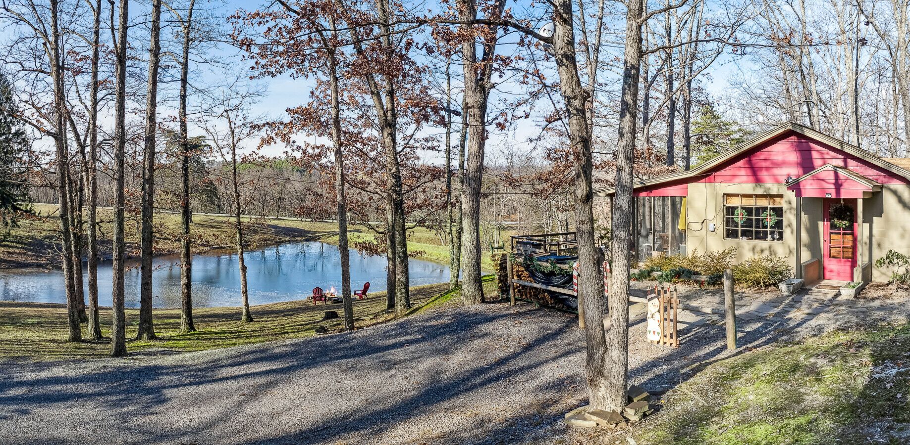 Une cabane avec un toit rouge, un étang et un espace aménagé pour faire un feu de camp.