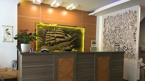 A reception desk with a ship mural, a potted plant, and a decorative partition. - Hoang Gia I Hotel Yen Xa - by Bay Luxury (Hanoi)
