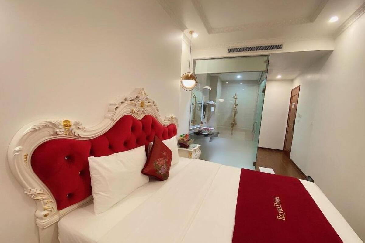 A hotel room with a red upholstered headboard, white bedding, and a red throw blanket.