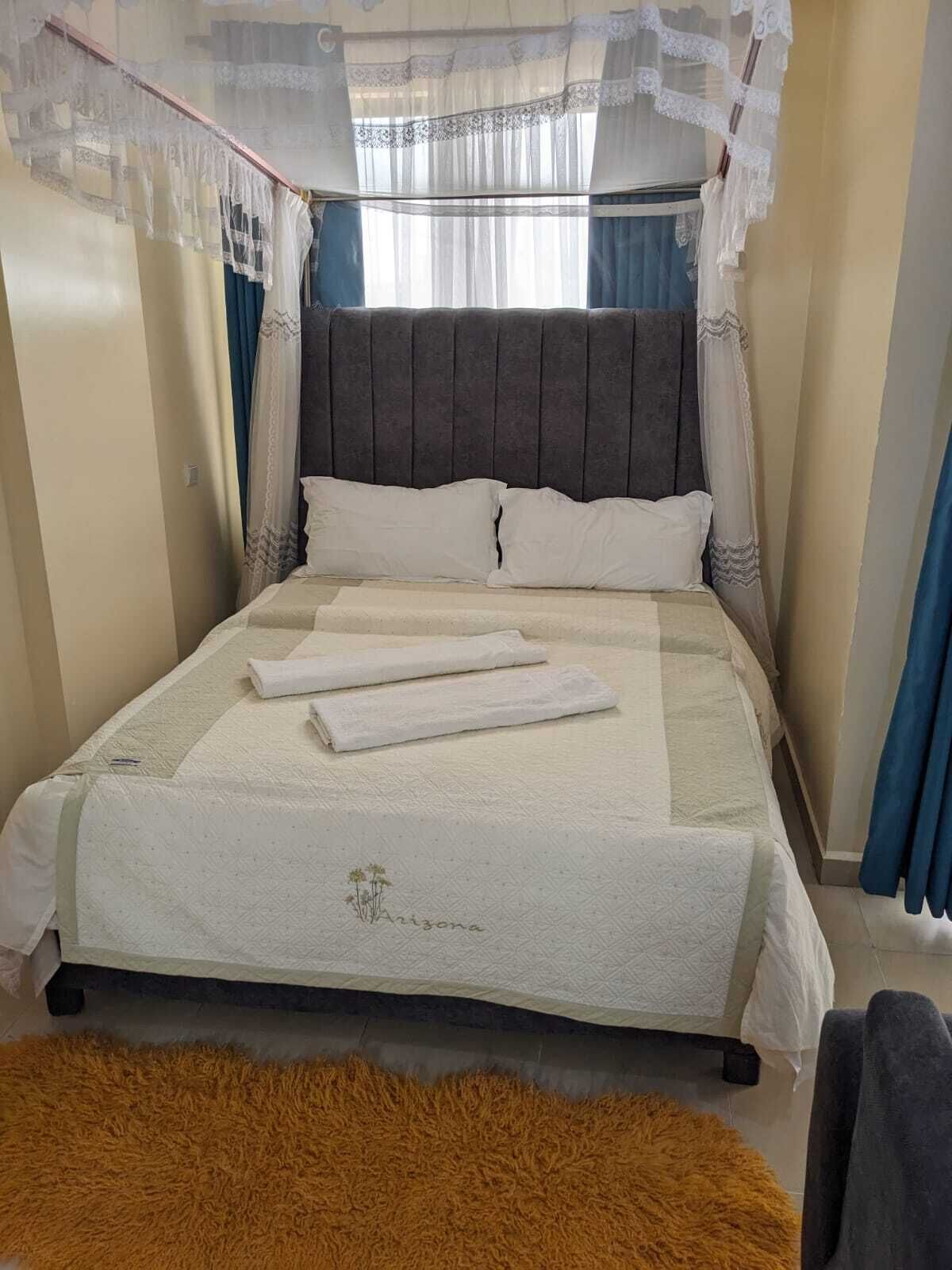 Un lit bien fait, avec une couverture matelassée, une tête de lit et un baldaquin agrémenté de détails en dentelle.