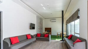 A modern living room with two grey sofas, each with a red cushion, a flat-screen TV mounted on the wall, and a wooden floor. - Terrazzo Suits (Ahmedabad)