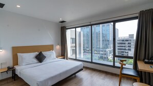 A hotel room with a large bed, a desk, and a view of the city through a large window. - Terrazzo Suits (Ahmedabad)