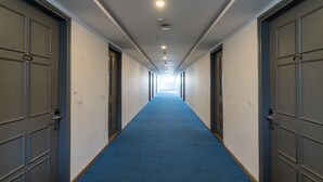 A long hallway with blue carpet, doors numbered 606 and 607, and a bright light at the end. - Terrazzo Suits (Ahmedabad)