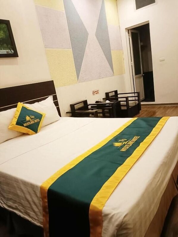 A hotel room with a bed, a pillow with the hotel logo, a desk, and a chair. - WestLake Trich Sai Hotel - by Bay Luxury (Hanoi)