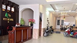 A reception desk with a logo, a clock, and a plant. There are motorcycles parked in the background. - WestLake Trich Sai Hotel - by Bay Luxury (Hanoi)