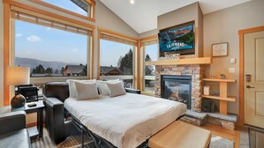 A spacious bedroom with a large bed, a fireplace, a TV, and a view of mountains.