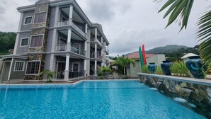 Un hotel de varios pisos con piscina, fachada de piedra y vistas a un paisaje montañoso.
