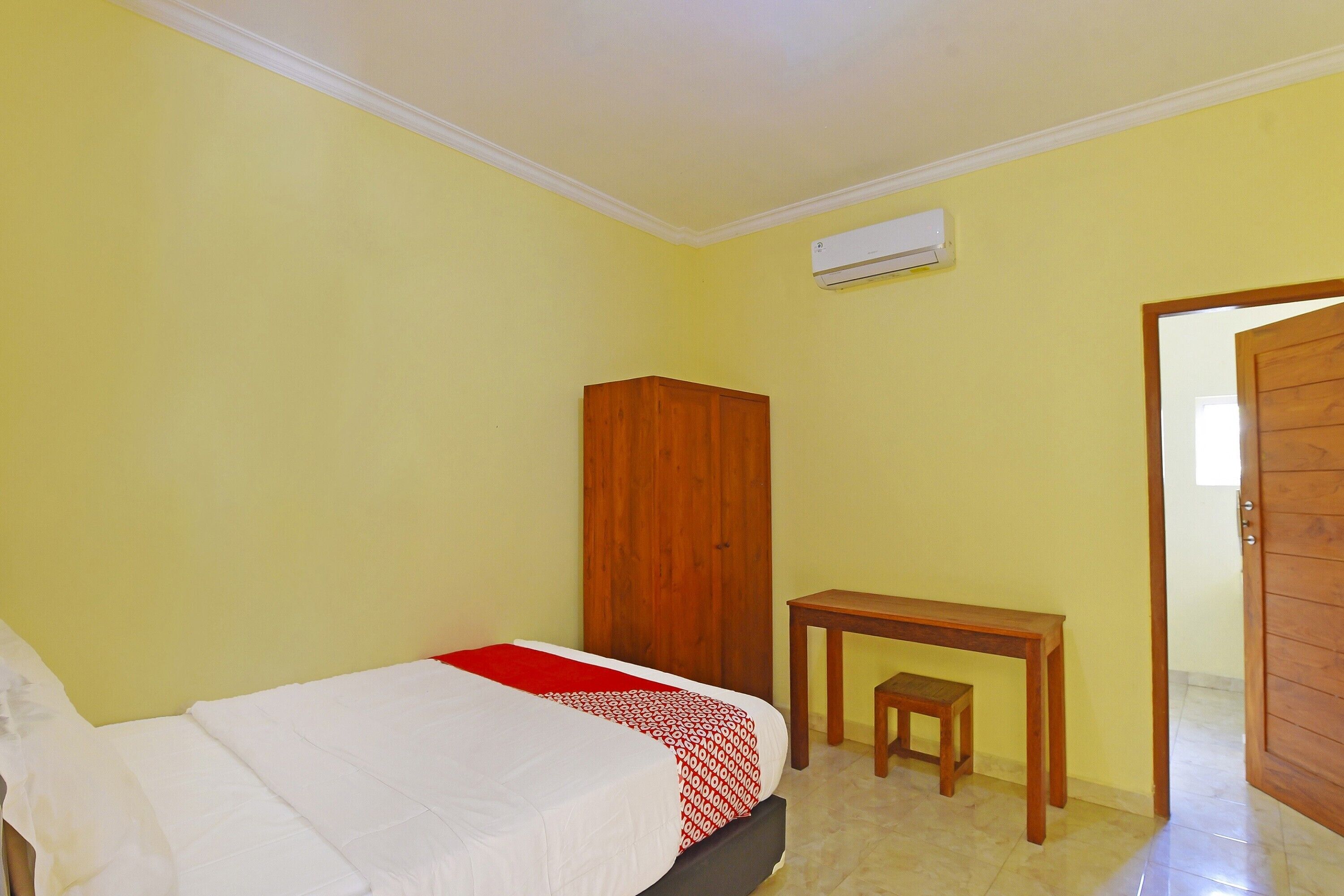 Un dormitorio con cama, un armario de madera, una mesita con banco y un equipo de aire acondicionado en la pared.