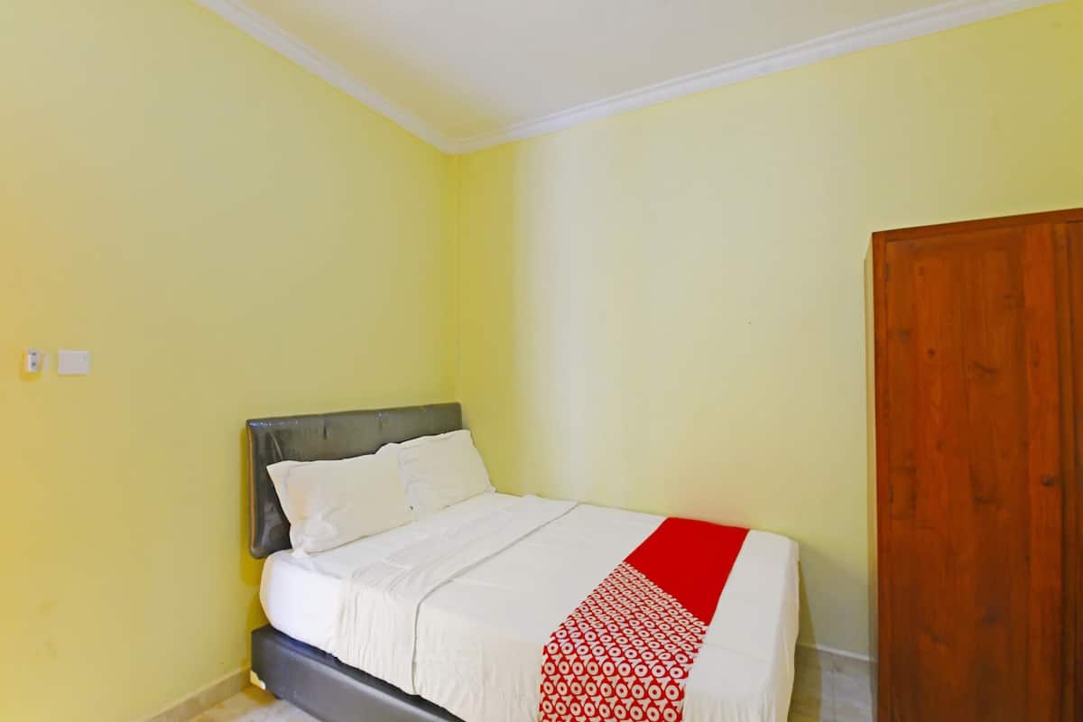 A single bed with a grey headboard and white bedding, a red and white patterned throw, and a wooden door to the right.
