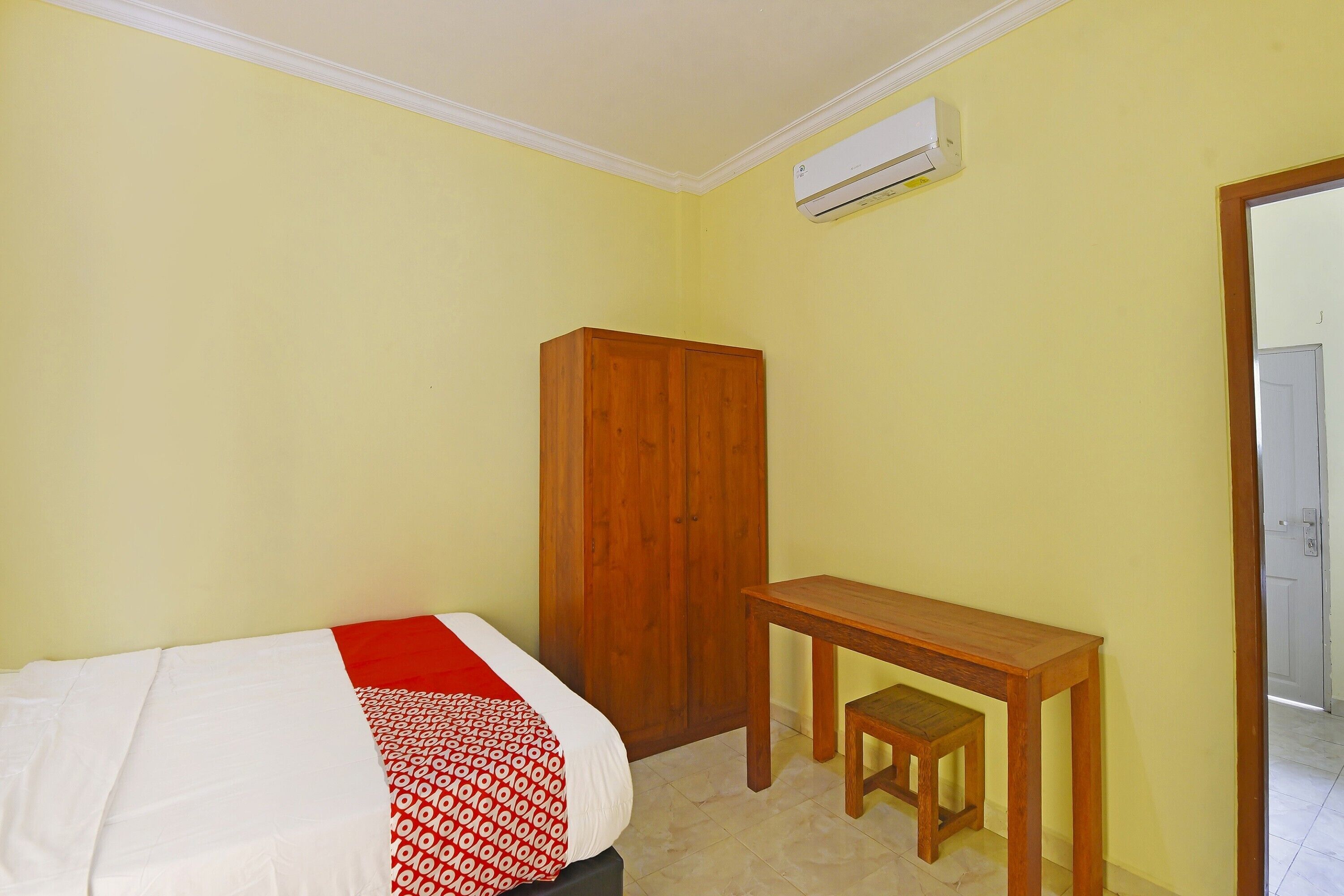 Une chambre à coucher avec un lit, une armoire en bois et une petite table en bois accompagnée d’une chaise.