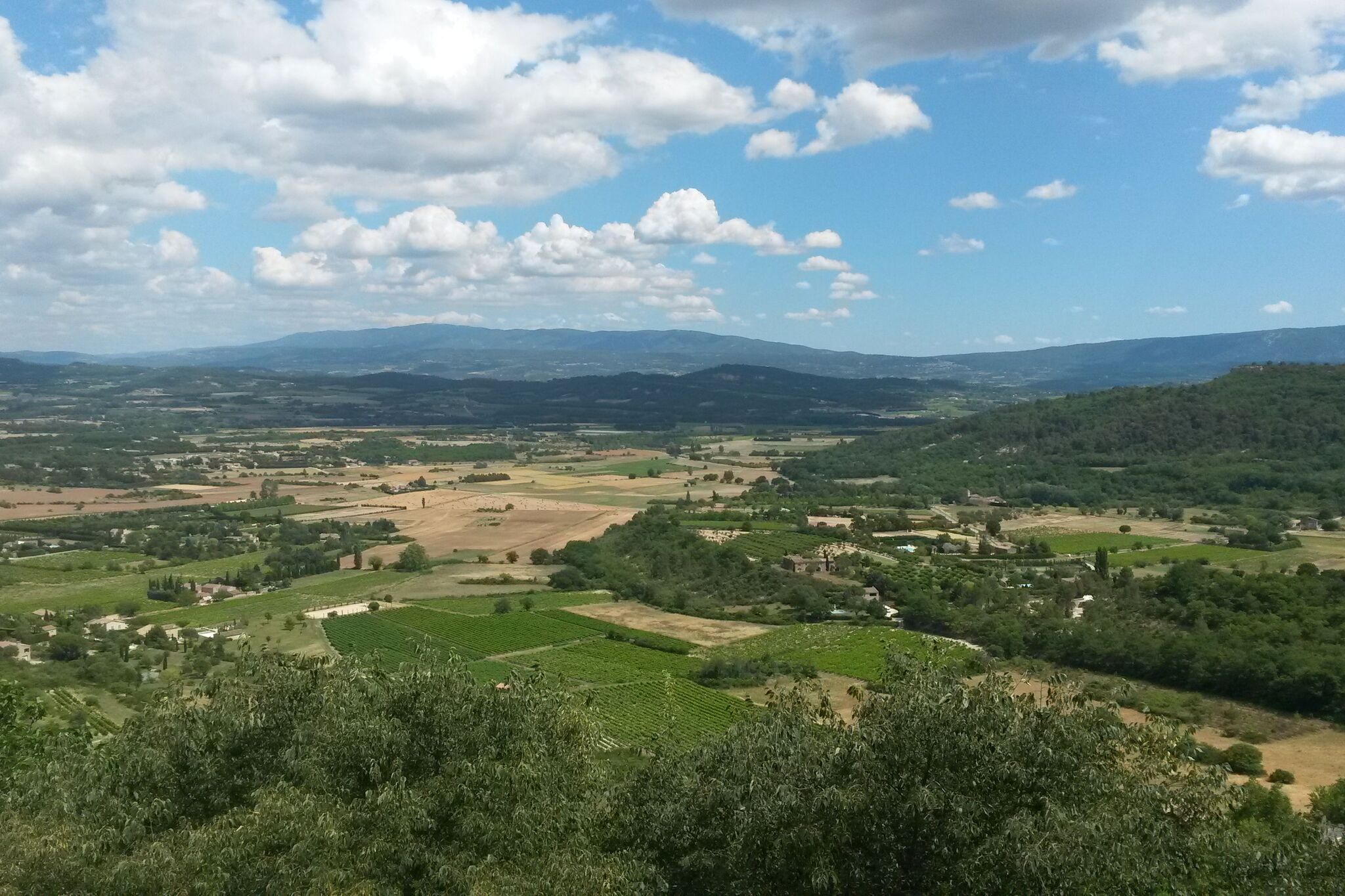 A panoramic view of a rural landscape with fields, scattered houses, and mountains in the distance.