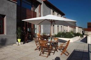 Une terrasse extérieure avec une table et des chaises, un grand parasol et des plantes en pot.