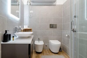 A modern bathroom with a white sink, bidet, and toilet, a mirror, and a shower area. - New and cozy Apartment in Center (Milano)