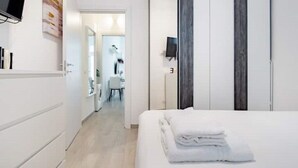 A hotel room with a bed, a TV, a bathroom with a mirror, and a door leading to another room. - New and cozy Apartment in Center (Milano)