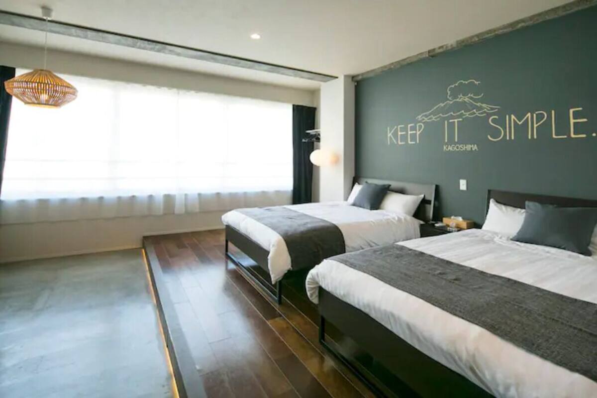 A modern hotel room with two beds, a large window, and a wall with a motivational quote.