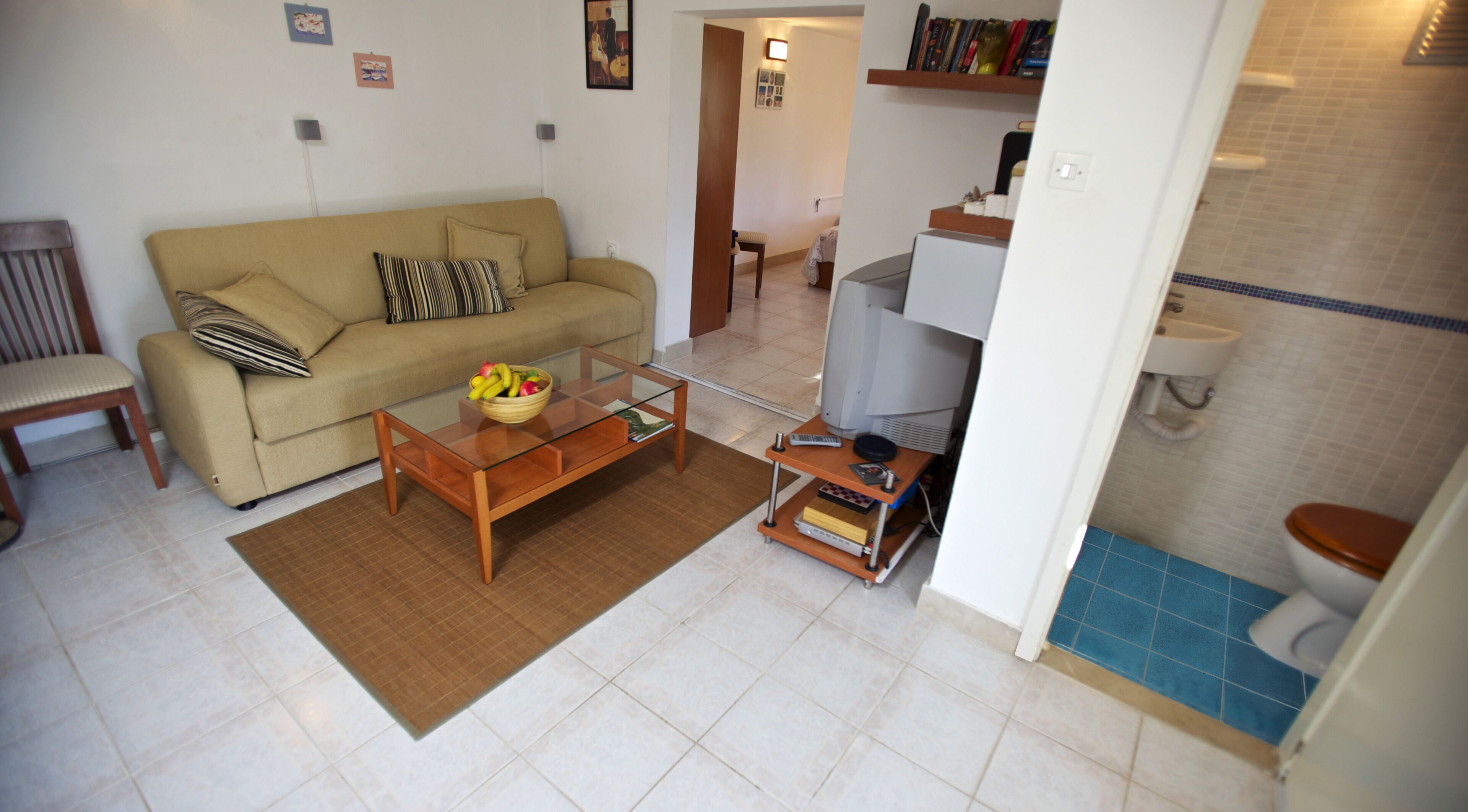A living room with a sofa, coffee table, and a small kitchen area with a refrigerator and sink.
