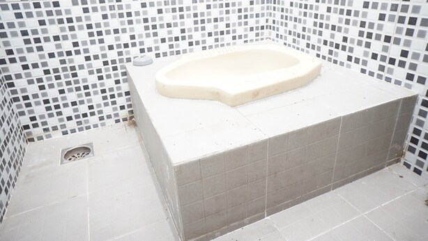 A bathroom with a white bathtub, tiled walls, and a drain. - OYO Life 93017 Kost H Soeroso (Situbondo)