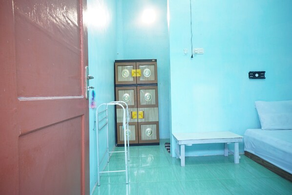 A room with a bed, a bench, a door, and a wall-mounted electrical outlet.