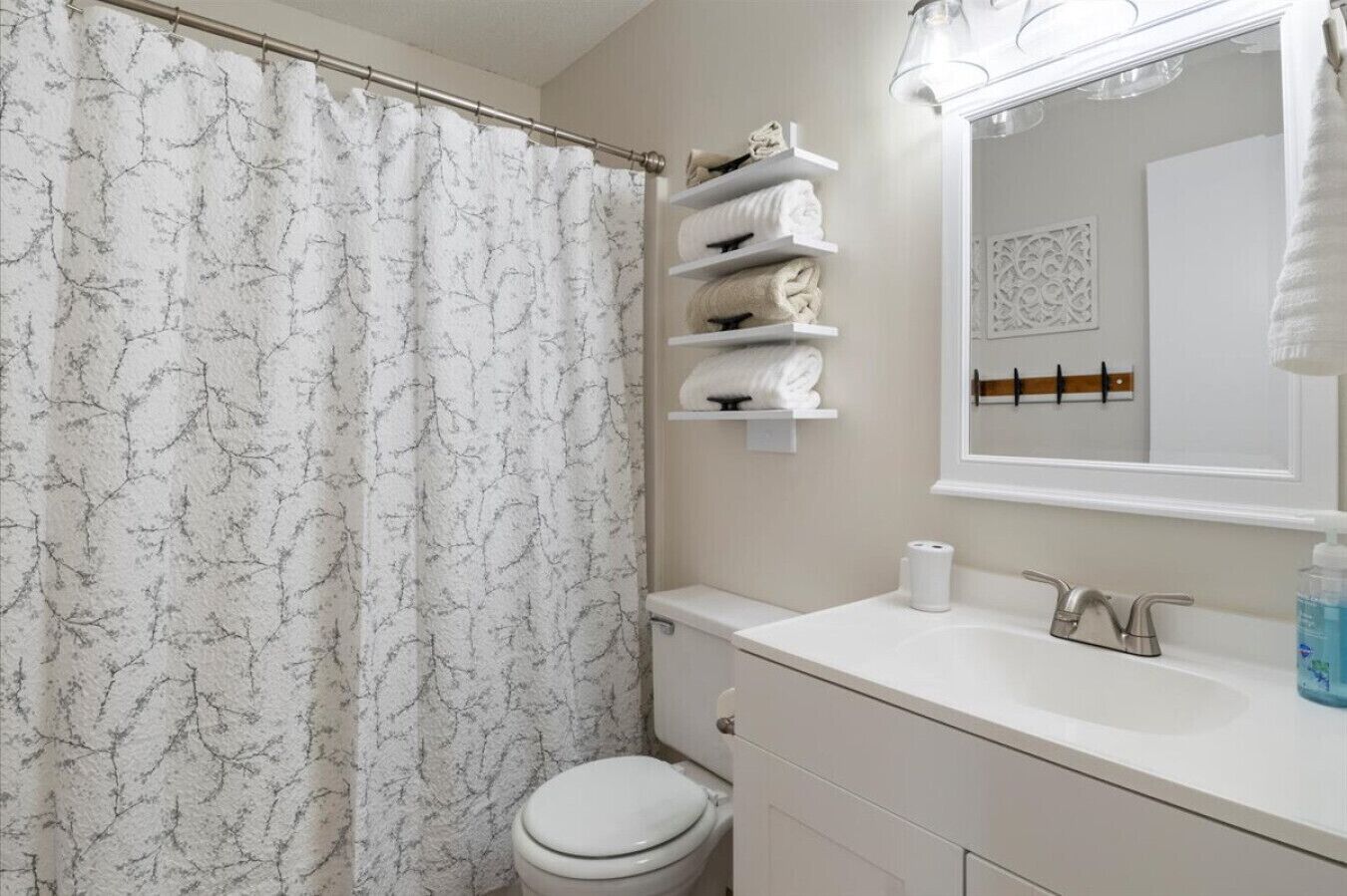 Een badkamer met een douchegordijn met marmerprint, een toilet, een wastafel met spiegel, en planken met opgevouwen handdoeken.
