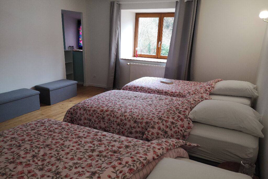A bedroom with two beds, a window, a radiator, and a small desk area.