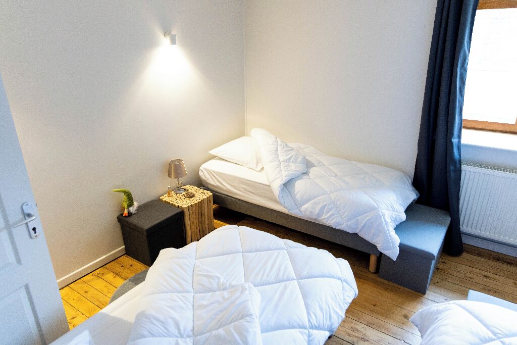 A small, modern bedroom with two beds, a bedside table, and a nightstand.