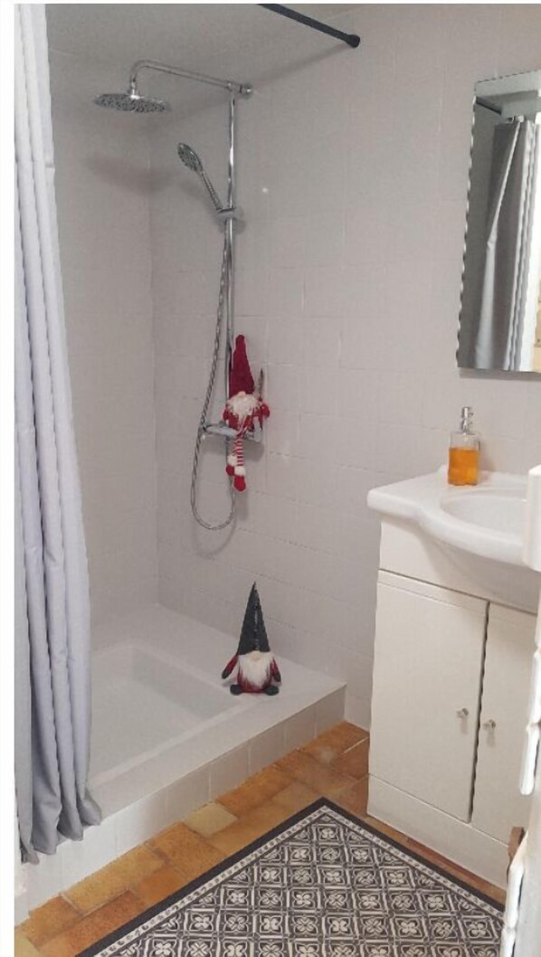Une salle de bain avec une douche, un lavabo et un petit gnome décoratif.